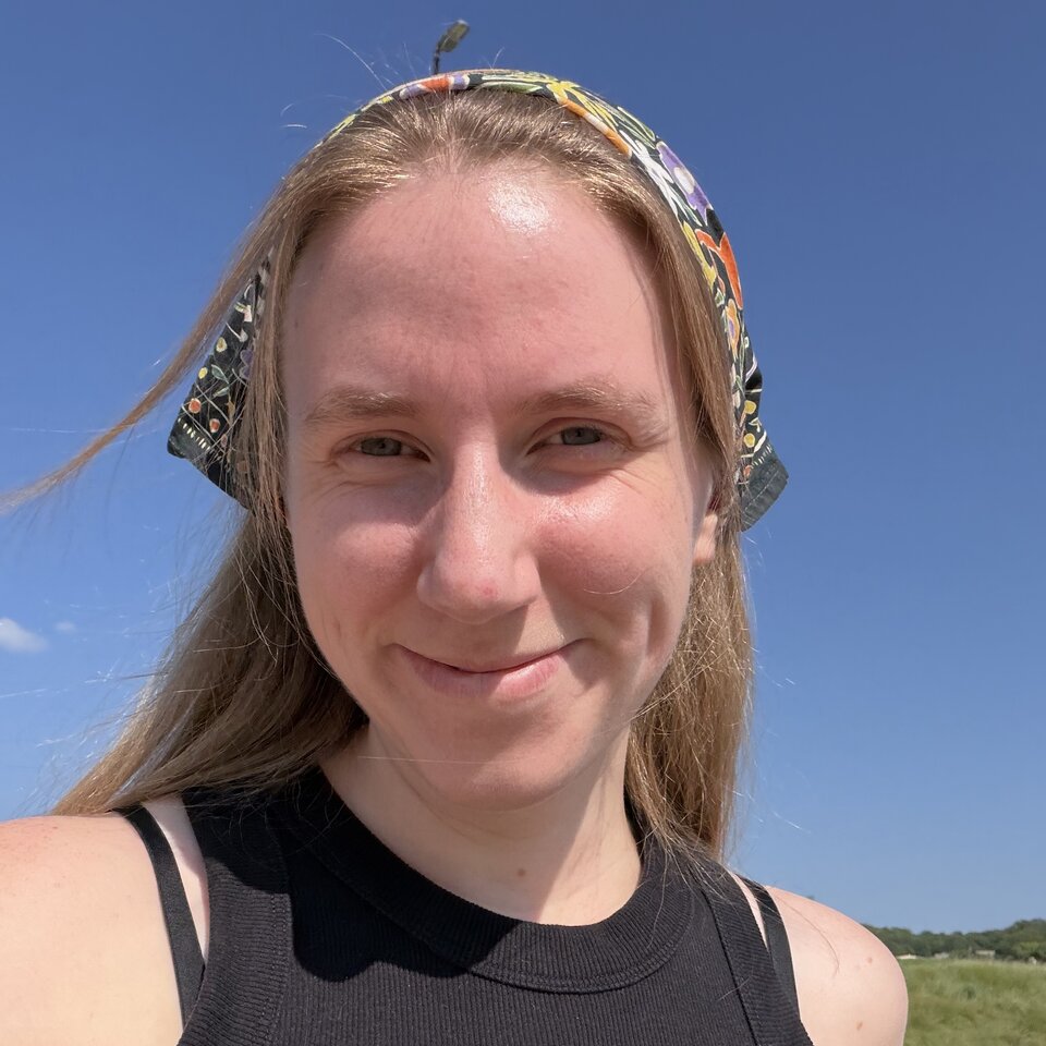 Smiling woman with a colorful headband outdoors under a bright blue sky.