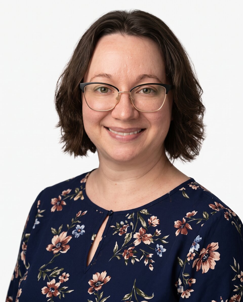 Smiling woman with glasses, wearing a floral navy blouse against a white background.